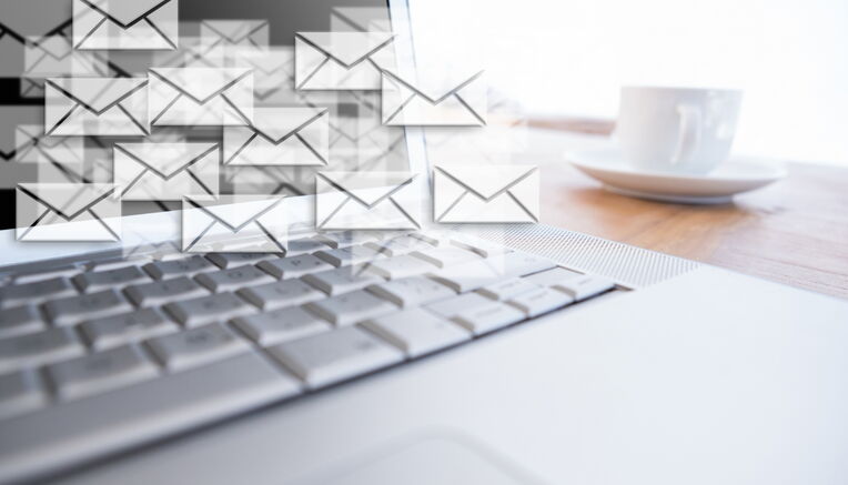 Eine Nahaufnahme einer Laptoptastatur mit vielen schwebenden E-Mail-Symbolen, die aus dem Bildschirm kommen, mit einer Tasse Kaffee im Hintergrund. Dies symbolisiert effektive Beste Praktiken für Outreach-E-Mails.