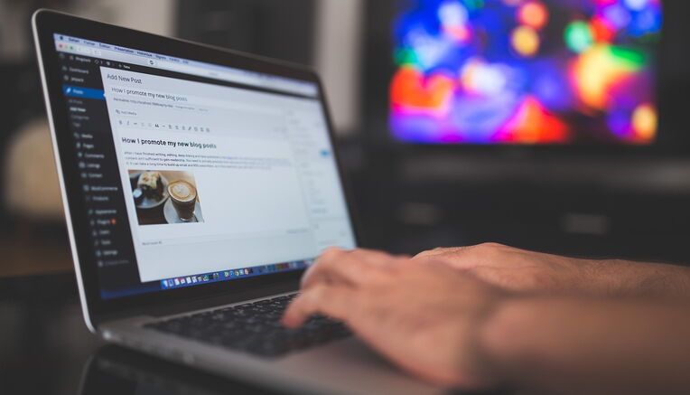 Laptop mit Blogging-Software, Hände tippen, bunter Bildschirm im Hintergrund