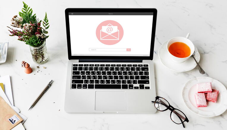 Eine Draufsicht auf einen Laptop mit einem E-Mail-Symbol auf dem Bildschirm, umgeben von einem Tee, Süßigkeiten und Schreibwaren auf einem sauberen Schreibtisch, was die Beste Praktiken für Outreach-E-Mails veranschaulicht.