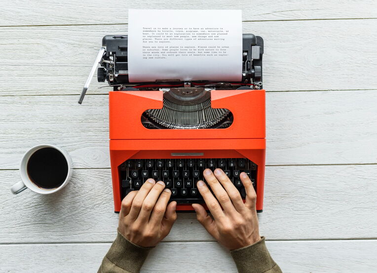 Person tippt auf einer roten Schreibmaschine, daneben steht eine Tasse Kaffee. Dies könnte den Prozess des Schreibens von Inhalten darstellen, auch für Blog-Kommentare, um Backlinks durch Blog-Kommentare generieren zu können.