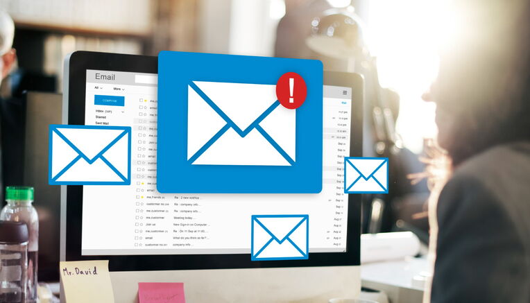 Eine Person, die an einem Computer arbeitet, auf dessen Bildschirm E-Mail-Symbole und eine E-Mail-Oberfläche mit einem Warnzeichen angezeigt werden. Dies zeigt die Bedeutung der Beste Praktiken für Outreach-E-Mails.