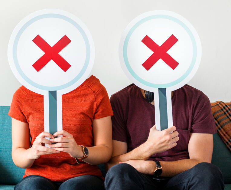 Zwei Personen sitzen mit Schildern vor dem Gesicht, die ein rotes X zeigen, was Ablehnung oder Fehler symbolisiert. Dies könnte darstellen, was man beim Versuch, Backlinks durch Blog-Kommentare generieren zu wollen, vermeiden sollte.